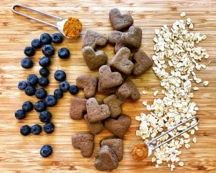 Earth Buddy Hemp Hearts treats with turmeric, blueberries, and oats on a wooden board. 