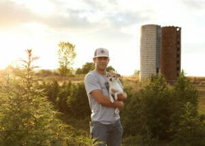 Co-founder of Colorado dog company Earth Buddy, Sean Zyer, holding a small dog in a hemp field