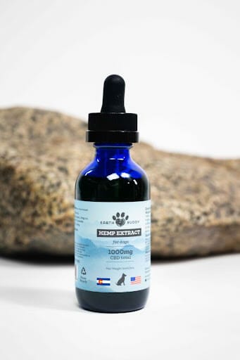 earth buddy 1000mg cbd oil for dogs in a blue bottle with light blue label in front of a rock with white background. 