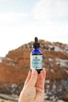 hand holding earth buddy 1000mg hemp extract for dogs in the rocky mountains. Full spectrum cbd contains omega 3 fatty acids shown to help dogs with irritated skin.