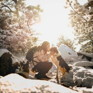 Man and black, white, and brown spotted dog in a snowy forest. Read this article to learn more about dog skin irritation.