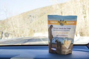 Earth Buddy CBD treats for dogs on the dashboard inside a car driving through the rocky mountains. Don’t leave home without our CBD treats for dogs when going on car rides. 