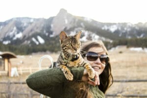 Tan bengal cat on the shoulders of a woman in the front range of rocky mountains. CBD for cats can ease anxiety and help with enrichment for felines. 