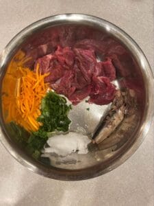 Metal dog food bowl with whole food ingredients like raw meat, veggies, sardines, and organic CBD oil for dogs. Daily CBD oil for dogs provides the best results. 