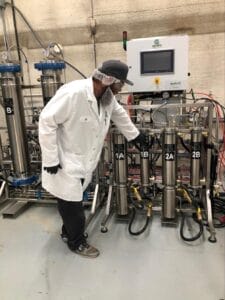 Man in white lab coat pointing to a supercritical Co2 extraction setup that is used to safely extract cannabinoids and terpenes from the cannabis plant.