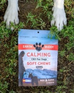 2 white dog paws next to a bag of Earth Buddy Grain Free dog calming chews with 10mg of full spectrum CBD for dogs. 