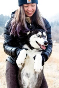 Woman holding up a Siberian Husky by the front paws in snowy Colorado. CBD balm for dog paws helps in the winter time.