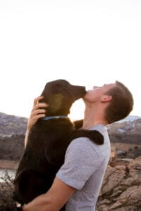 Man holding his black labrador retriever and giving him a kiss. Earth Buddy makes the best natural supplements for dogs.