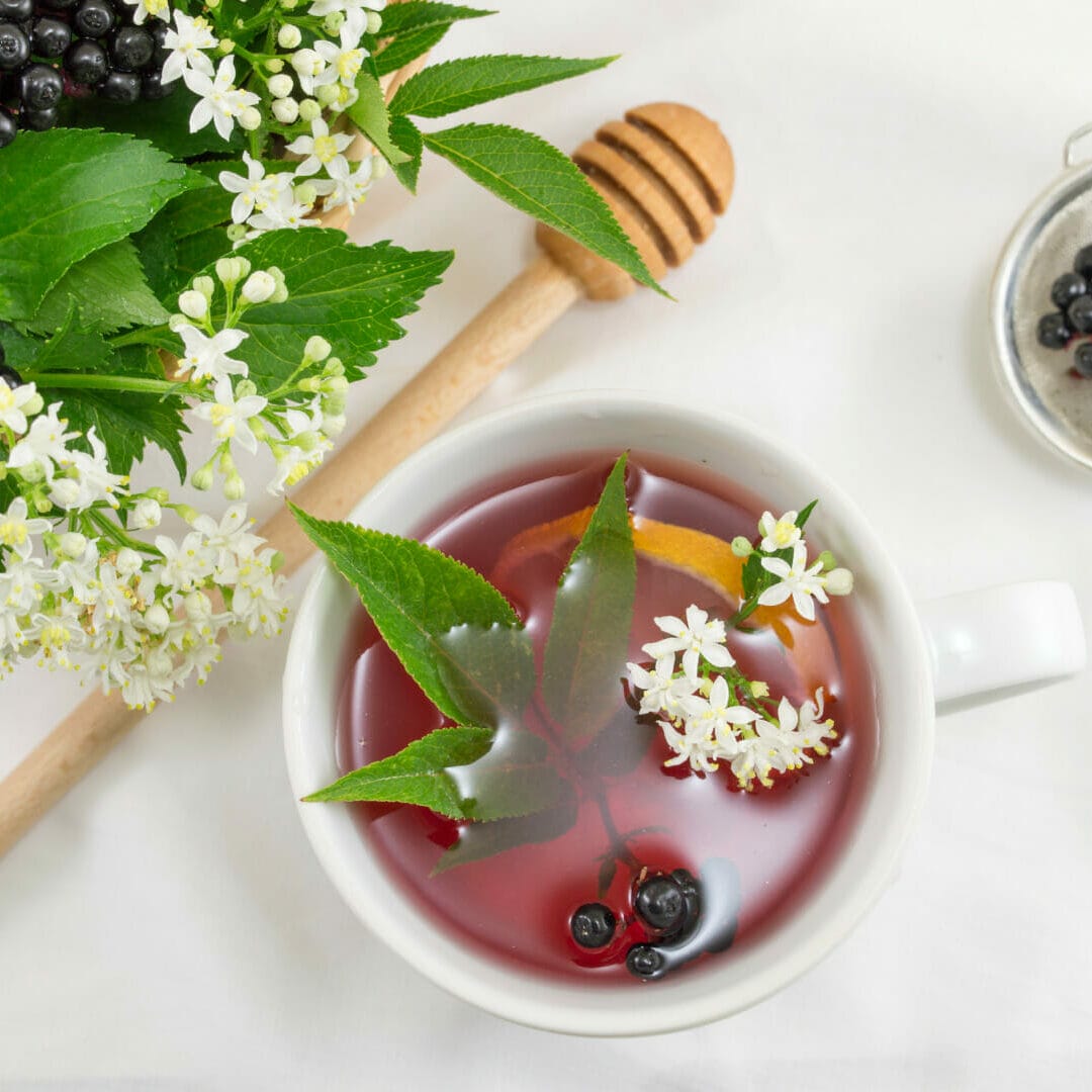 image of elderberry flower, berries, and elderberry extract in a bowl with kitchen utensils. Elderberries are high in vitamin C and quercetin.