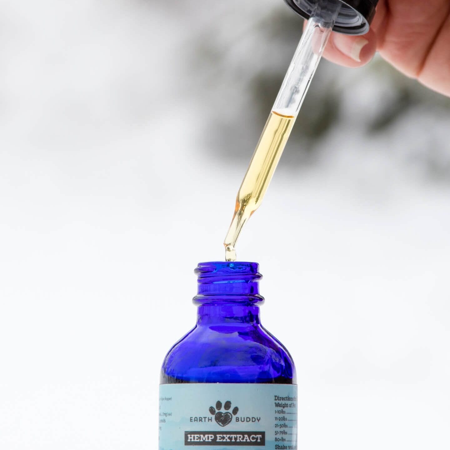 Hand squeezing a dropper into a bottle of Earth Buddy Organic CBD Oil for dogs. You can mix cbd oil into food with ease.